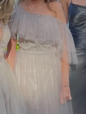 Ljus offshoulder långklänning med glitter - Säljer en ljus, glittrig långklänning med offshoulder och volangdetalj upptill. Perfekt för bal! Endast använd en gång i superfint skick från Ida Sjöstedt 