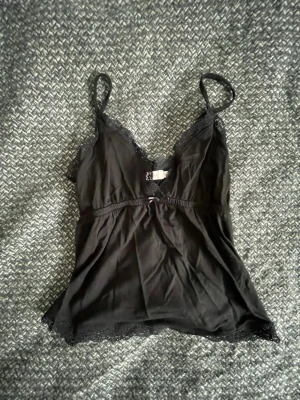 Svart spetsnattlinne från Nelly - Säljer ett svart nattlinne från Nelly i storlek XS. Nattlinnet har tunna axelband, spetsdetaljer vid urringningen och nederkanten samt en mjuk, följsam passform. Perfekt för mysiga kvällar hemma.