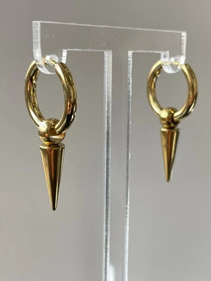 Guldiga hoops med konformad detalj - Snygga örhängen i guld,  rostfri stål med rund hoop och hängande konformad detalj. Designen är minimalistisk men edgy, perfekt för dig som gillar statement-accessoarer. Passar till många olika stilar och ger en cool touch till din look.