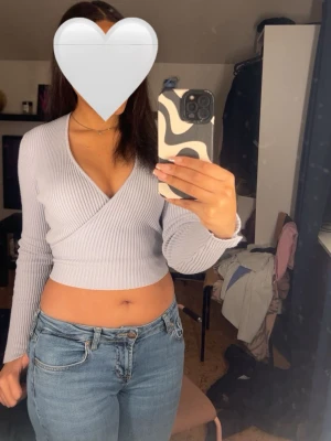 Ljuslila omlottopp från Zara - Säljer en ljusblå ribbad omlottopp från Zara. Toppen är croppad med lång ärm och har en snygg v-ringning. Den har långa snören som man kan knyta hur man vill 