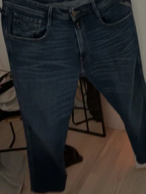 Blå jeans från Replay - Säljer ett par klassiska blå jeans från Replay med fem fickor och raka ben. Jeansen har snygga slitningar och detaljerade sömmar. Tillverkade i slitstarkt denimtyg som ger en cool och tidlös look.