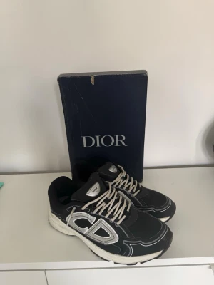 Svarta sneakers b30 - Snygga svarta sneakers med vita och grå detaljer samt vita skosnören. Skorna har en chunky sula och tydlig CD på sidan. Tillverkade i en mix av textil och läder för en exklusiv känsla. Perfekta för dig som vill sticka ut med stil.