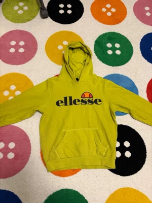 Gul hoodie från Ellesse - Cool gul hoodie från Ellesse med stor logga framtill. Klassisk huva och känguruficka gör den både snygg och praktisk. Perfekt för dig som vill sticka ut med färg och sportig stil. Mjuk och skön känsla tack vare bomullsmaterial.
