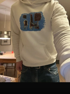 Vit hoodie med konstmotiv Les Deux - Säljer en stilren vit hoodie från Les Deux med ett unikt konstmotiv i blått, brunt och svart på bröstet. Perfekt för dig som gillar streetwear/ archive stil och konstnärliga detaljer.                      Nypris 800kr, Mitt pris 329kr! Nytt skick