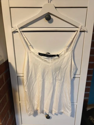 Vit linne med spets - Snygg vit linnetopp från Lager157 i storlek L. Toppen har tunna axelband och v-ringad hals med fin spetskant. Perfekt att styla till jeans eller kjol för en fräsch look.