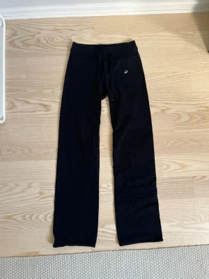 Svarta mjukisbyxor från  - Säljer ett par svarta mjukisbyxor med raka ben och dragsko i midjan. Byxorna har en liten logga på höften och är tillverkade i mjukt, stretchigt material som passar perfekt för chill eller träning.