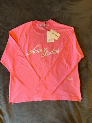 Rosa långärmad tröja Acne Studios - Snygg rosa långärmad tröja från Acne Studios med broderad logga i vitt framtill. Tröjan har rund halsringning och är gjord i mjukt bomullsmaterial. Perfekt för dig som vill ha en trendig och bekväm look.