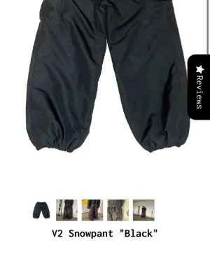 Svarta V2 Snowpant täckbyxor Threads - Säljer ett par svarta V2 Snowpant täckbyxor med bred passform och resår vid benslut. Perfekta för vintern och riktigt snygga till streetwear-looken. Byxorna har praktiska fickor och är gjorda i ett slitstarkt material som står emot kyla och snö.