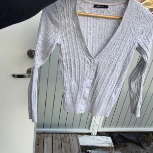 Ljusgrå ribbad omlottkofta Gina Tricot - Snygg ljusgrå omlottkofta från Gina Tricot med ribbad struktur och v-ringad hals. Koftan har lång ärm och är perfekt att slänga över en topp för en chill men ändå stilren look.passar xs-s