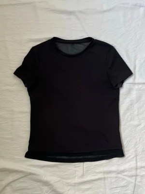 Svart sportig t-shirt med öppen rygg - Svart t-shirt i syntetmaterial med korta ärmar och rund hals. Baksidan har en cool öppen rygg-detalj med en liten reflekterande remsa upptill. Perfekt för träning eller när du vill ha en luftig och bekväm look. Använd fåtal gånger. Diskuterar gärna pris! 