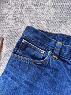Nudie jeans dry selvage - Snygga mörkblå jeans med raka ben och klassiska kontrastsömmar. Jeansen har fem fickor och silverfärgade nitar. Perfekta för en avslappnad och trendig look. Tillverkade i denim med en autentisk känsla.