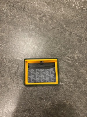 Svart korthållare  - Stilren svart korthållare med klassiskt mönster i vitt och grått. Tillverkad i läder och canvas, perfekt för kort och sedlar. Kommer i original ask med gul insida!