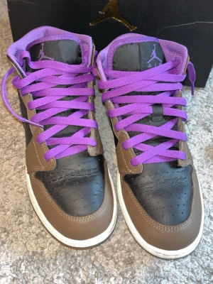 Air Jordan 1 med lila detaljer - Snygga Air Jordan 1 sneakers med lila skosnören och detaljer, svart och grå ovandel samt klassisk Nike-sula. Ikonisk Jumpman-logga på plösen och robust design. Perfekta för dig som vill sticka ut med färg och stil. Priset går att diskutera! Skickar inom 24h🙌🏻