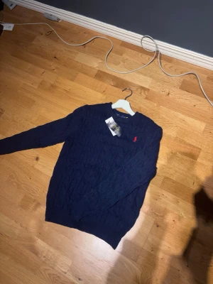Mörkblå kabelstickad tröja Polo Ralph Lauren - Mörkblå kabelstickad tröja från Polo Ralph Lauren, riktigt stilren och riktigt skönt material, perfekt för kyliga sommar kvällar! Tveka inte på att ställa frågor, eller diskutera😀
