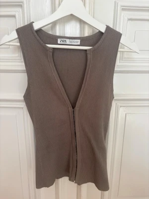 Populär stickad topp från Zara - Snygg ribbad brun ärmlös topp från Zara med djup v-ringning och knäppen fram till. 