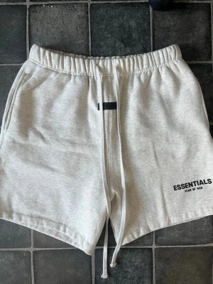 Essentials shorts - Snygga ljusgrå shorts från Essentials Fear of God med elastisk midja och dragsko. Tillverkade i mjuk bomull och har diskret logga tryckt framtill. Perfekta för en avslappnad och trendig stil.  OBS: Köpt på marknad så vet ej om autenticitet
