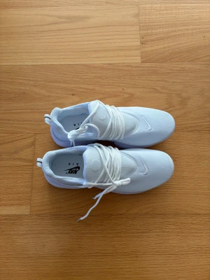 Nike Air vita sneakers - Fräscha helvita Nike Air sneakers med låg profil och klassisk siluett. Skorna har mesh-överdel för bra andningsförmåga, vita snören och diskret Nike-logga på sidan. Perfekta för dig som gillar stilrena och sportiga sneakers.