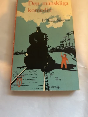 Den mänskliga komedin av Saroyan - Säljer boken 'Den mänskliga komedin' av William Saroyan. Omslaget är blått med en stor svart siluett av ett tåg och en person i orange som vinkar. Pocketformat med orange rygg och tydlig titel. Perfekt för dig som gillar klassisk skönlitteratur.
