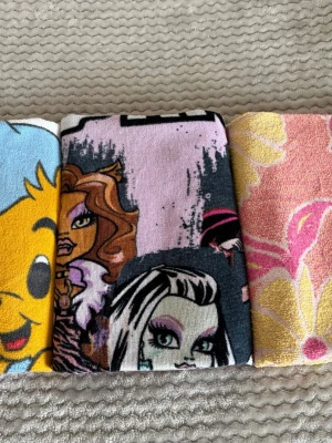 Tre färgglada barnhanddukar - Säljer tre olika barnhanddukar med motiv: en med Bamse, en med Monster High och en med blommor i rosa och gult. Handdukarna är mjuka och perfekta för stranden eller badet. Alla är i frotté och har färgglada tryck. 3st  Mått 50*130 75*130 70*130
