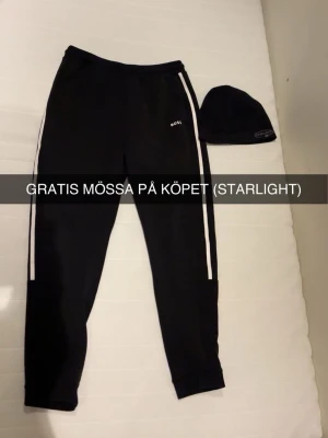 Svarta mjukisbyxor med vita ränder BOSS - Säljer ett par svarta mjukisbyxor från BOSS med vita ränder längs sidorna och diskret logga på låret. Byxorna har resår i midjan och muddar vid bensluten. Perfekta för chill dagar eller träning. GRATIS STARLIGHT MÖSSA PÅ KÖPET NO SIZE 