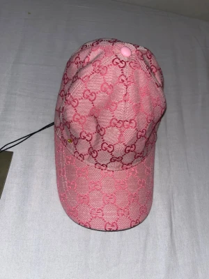 Rosa keps - Säljer en snygg rosa keps  med det klassiska monogrammet i mörkare rosa över hela kepsen. Kepsen har böjd skärm och justerbar baksida. Materialet är canvas med en lyxig känsla. Perfekt för dig som vill sticka ut med en trendig accessoar.