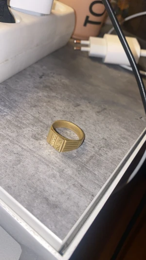 Guldring 18k - Snygg klackring med bred design och graverat geometriskt mönster på ovansidan. Ringen har en matt finish och stämplar på insidan som tyder på äkta guld. Perfekt för dig som gillar stilrena accessoarer med en unik touch.
