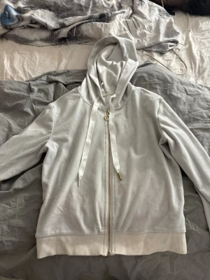 Vit hoodie med dragkedja - Snygg vit hoodie i mjukt material med dragkedja framtill och breda ribbade muddar. Luvan har breda snören med gulddetaljer. Perfekt för en chill och avslappnad stil.
