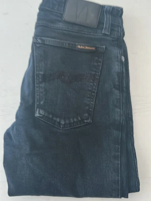 Svarta nudiejeans slimfit - Snygga svarta slim fit jeans med klassisk femficksdesign och svarta detaljer. Jeansen har en diskret logga på bakfickan och är tillverkade i mjukt denimtyg med stretch för extra komfort.
