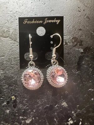 Silvriga örhängen med rosa sten - Snygga örhängen med rund, facetterad rosa sten infattad i en silvrig ram med små detaljer. Krokar i metall för enkel användning. Perfekta för att ge din look lite extra bling och färg.