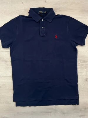 Ralph lauren pike mörkblå - Säljer en stilren mörkblå piké från Ralph Lauren. En klassisk och tidlös modell som passar lika bra till vardags som på sommaren eller vid lite finare tillfällen.  • Storlek: M • Färg: Mörkblå • Skick: Mycket fint skick • Broderad Ralph Lauren-logga på bröstet • Mjuk och bekväm passform • Perfekt att matcha med jeans, chinos eller shorts • Ett stilrent basplagg som aldrig går ur mode