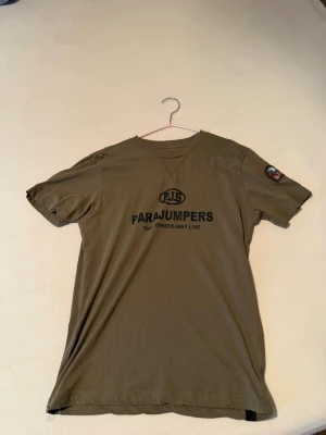 Olivgrön Parajumpers t-shirt - Snygg olivgrön t-shirt från Parajumpers med tryck på bröstet och patch på ärmen. Klassisk rund hals och korta ärmar. Perfekt för en avslappnad och cool stil.