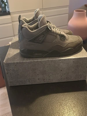 Air Jordan 4s Wet Cement - Snygga grå air Jordan 4s sneakers med hög siluett och detaljer i mocka och mesh. Skorna har en robust sula och coola plastdetaljer vid snörningen. Perfekta för dig som gillar streetwear och vill ha en stilren look.