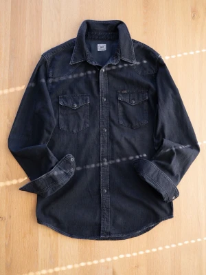 Svart Western jeansskjorta från Lee - Snygg svart jeansskjorta från Lee med två bröstfickor och tryckknappar framtill. Skjortan har klassisk krage och långa ärmar med knapp vid manschetten. Perfekt för en avslappnad och cool stil.