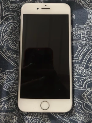 Vit iPhone med rund hemknapp - Säljer en stilren vit iPhone med klassisk rund hemknapp och snyggt glas på både fram- och baksida. Telefonen har en kamera med blixt på baksidan och Apples logga i mitten. Perfekt för dig som gillar enkel och modern design, det är en iPhone 8 som är i jätte bra skick den är bara lite skråmig.😍