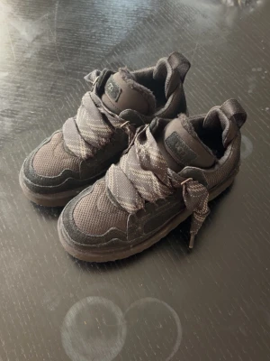 Bruna sneakers med breda snören - Snygga bruna sneakers med breda, mönstrade snören och meshdetaljer. Skorna har lågt skaft och vadderad plös samt krage för extra komfort. Ovandelen är i textil och mockaliknande material, perfekt för en trendig streetstyle.