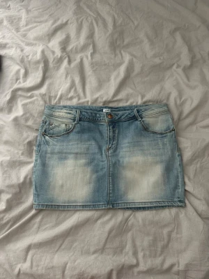 Ljusblå jeanskjol med fickor - Säljer en ljusblå kort jeanskjol med slitna detaljer och klassiska fem fickor. Kjolen har bälteshällor, knapp och dragkedja framtill samt två bakfickor. Perfekt till en avslappnad och trendig look.