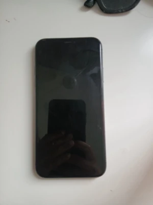 Svart iPhone 11 med dubbla kameror - Säljer en svart iPhone 11 i befintligt skick med stilren design och rundade kanter. Telefonen har en baksida i glas, dubbla kameror och Apple-loggan i mitten. Perfekt för dig som gillar snygg och modern teknik. Den har inga sprickor på varken fram eller baksida. Fungerar precis som ny. På övre framsida display har den tre  svarta streck.
