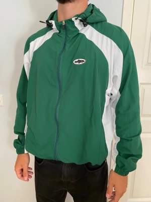 corteiz windbreaker  - Snygg Corteiz windbreaker jacka i storlek TTS L, avslappnad passform. Personen på bilden är ca 185cm lång och väger 90kg