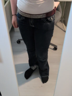 Vinrött nitarbälte med silverdetaljer - Säljer ett vinrött bälte med silverfärgade nitar i två rader längs hela bältet. Bältet har en klassisk form och passar perfekt för att ge din outfit en edgy touch. Materialet är syntet och bältet har ett coolt, trendigt uttryck.