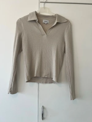 Beige ribbstickad tröja från ONLY - Snygg beige ribbstickad tröja från ONLY med krage och v-ringning. Med lite längre armar och mjukt material! 