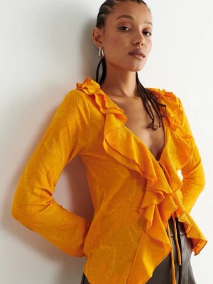 Orange volangkofta med blommönster - Snygg orange kofta med volangkant och blommönster i tyget. Koftan är tunn och har knytband framtill, perfekt för att ge outfiten lite extra färg. Lätt transparent material och långa ärmar.
