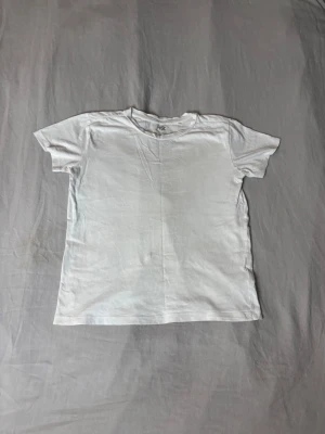 Klassisk vit t-shirt i bomull - En enkel och stilren vit t-shirt med rund hals och korta ärmar. Tillverkad i mjuk bomull som känns skön mot huden. Perfekt basplagg att matcha med allt i garderoben.