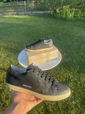 Golden goose - Snygga svarta sneakers med vit sula och stjärndetalj på sidan. Skorna har svarta skosnören och en diskret text på sidan. Hälpartiet har en glittrig detalj som ger extra stil. Perfekta för dig som gillar en clean och trendig look.