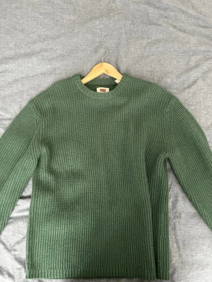 Grön stickad tröja från Levi's - Mysig grön stickad tröja från Levi's i relaxed fit. Tröjan har rund halsringning, ribbstickad struktur och långa ärmar. Perfekt för lager på lager och enkel att matcha med jeans eller kjol.