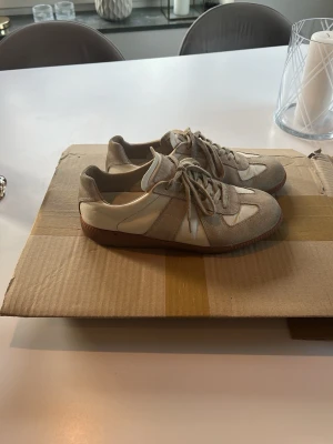 Maison margiela vita/grå randiga sneakers  - Tjena säljer mina skor nu och försöker få sålt ganska snabbt, Snygga sneakers i beige/grå mocka och vitt skinn med klassisk retrodesign. Perfekta för dig som gillar stilrena och tidlösa sneakers med låg profil. Om ni är intresserade skriv gärna!! 