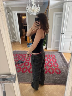 Rutiga pyjamasbyxor i grönt och svart - Säljer ett par rutiga pyjamasbyxor i grönt, svart och vitt med dragsko i midjan. Byxorna har en avslappnad passform och är perfekta för mysiga hemmakvällar. Materialet är mjukt och bekvämt, 100% bomull ekologiskt 