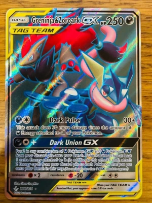 Trade Pokémonkort Greninja & Zoroark GX - Säljer ett holografiskt Pokémonkort med Greninja & Zoroark GX Tag Team. Kortet har färgstark design med svart, blått och rött motiv. Perfekt för samlare eller Pokémon TCG-spelare som vill ha en cool och kraftfull Tag Team-kombination.