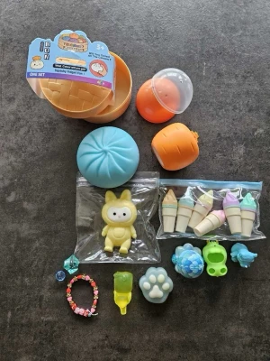 Sött mixat kit med små accessoarer squishy  - Ett färgglatt kit med små accessoarer och dekorationer, inklusive en blå squishy bulle, isglassar i pastellfärger, ett gult djur i plast, pärlarmband, samt små figurer och berlocker. Perfekt för att dekorera väskor, mobil eller använda som nyckelringar.