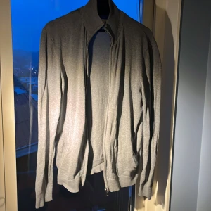 Grå cardigan jacka från Pier One - Grå cardigan jacka från Pier One med ribbad krage och muddar. Jackan har dragkedja framtill och är långärmad. Materialet är mjukt och känns som bomull, perfekt för chill dagar. Enkel och stilren design utan mönster.