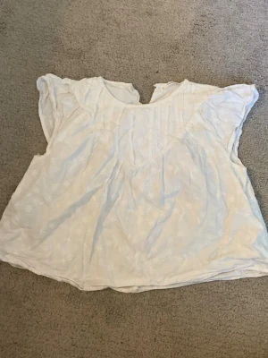 Vit blus med broderade detaljer - Söt vit blus med broderade blommor och lös passform. Blusen har korta ärmar och en lätt, luftig känsla som passar perfekt till varma dagar. Enkel att matcha med både jeans och kjol.